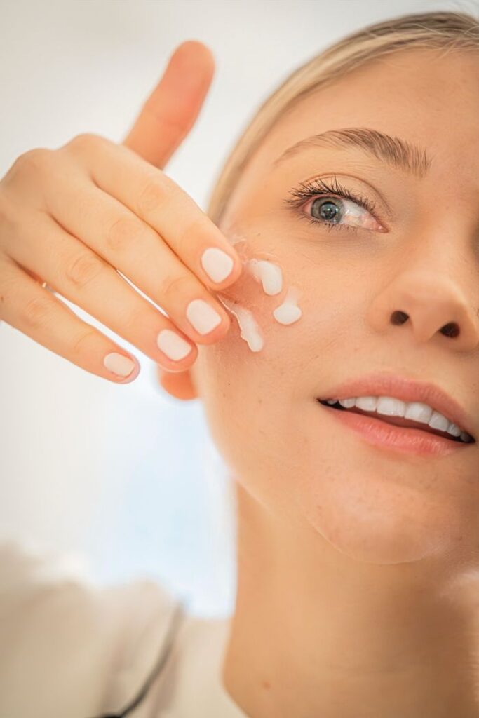Close-up of a woman's face applying moisturizer, showcasing skincare routine and healthy skin.