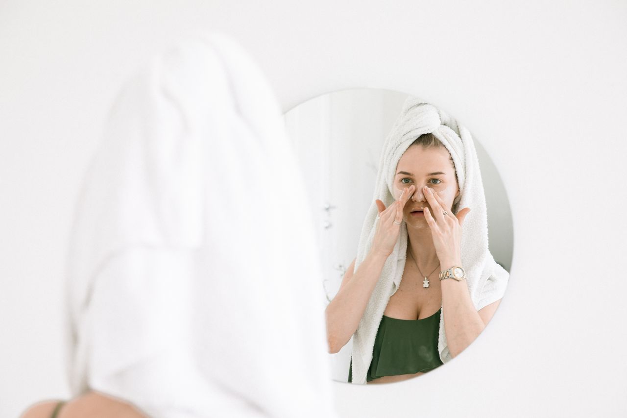 Crafting Captivating Headlines: Your awesome post title goes here A woman in a towel performing her skincare routine in front of a bathroom mirror.