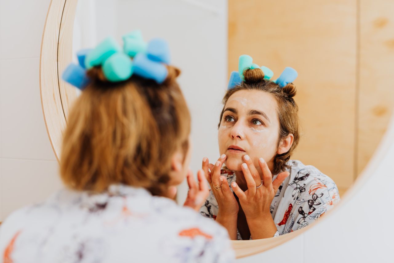 Mastering the First Impression: Your intriguing post title goes here Woman with curlers applying cream in front of a mirror indoors.