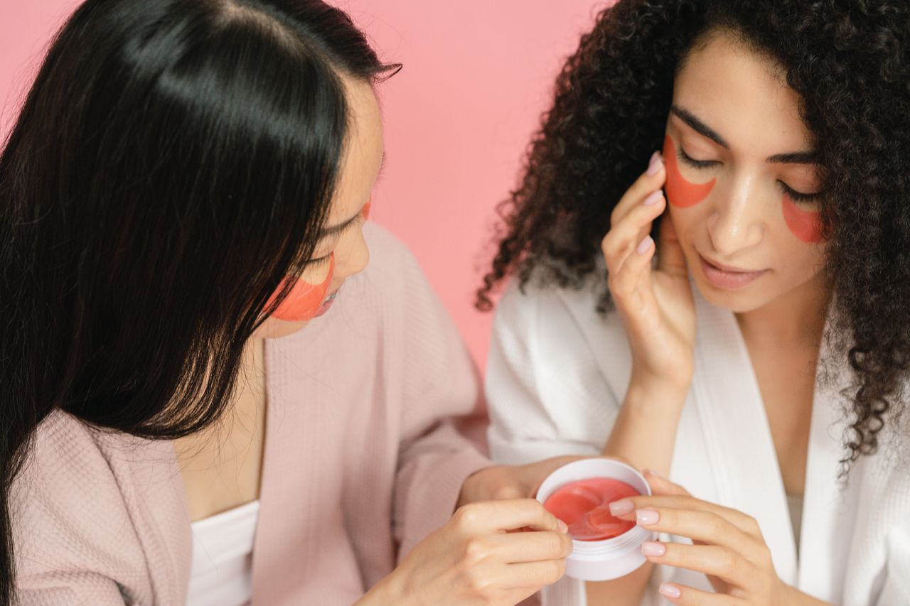 The Art of Drawing Readers In: Your attractive post title goes here Two women applying red eye patches in a skincare routine, focusing on beauty and self-care.
